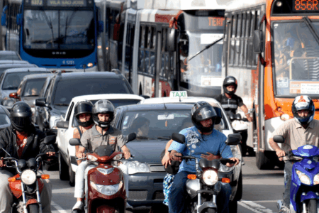 motos e carros lado a lado em rua movimentada